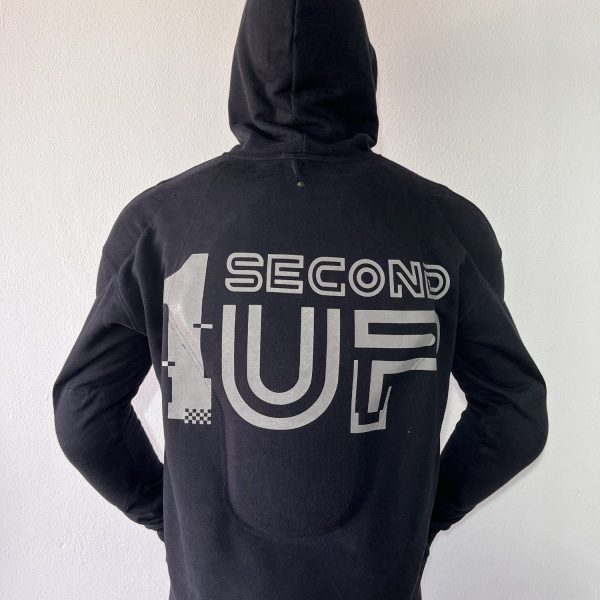 Back view of a Second 1UP black motorcycle hoodie with a large reflective logo logo for visibility, worn by a motorsports rider in a helmet