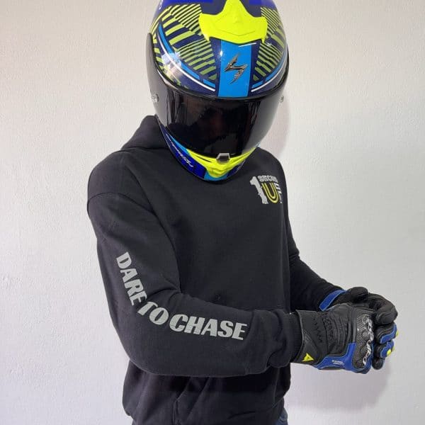 Side view of a Second 1UP black motorcycle hoodie with 'Dare to Chase' text on the sleeve, worn by a motorsports rider in a helmet