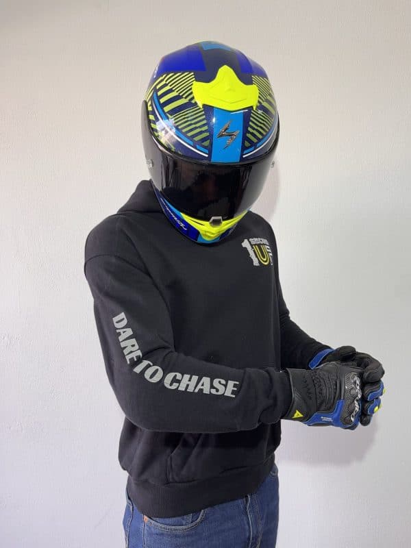 Side view of a Second 1UP black motorcycle hoodie with 'Dare to Chase' text on the sleeve, worn by a motorsports rider in a helmet