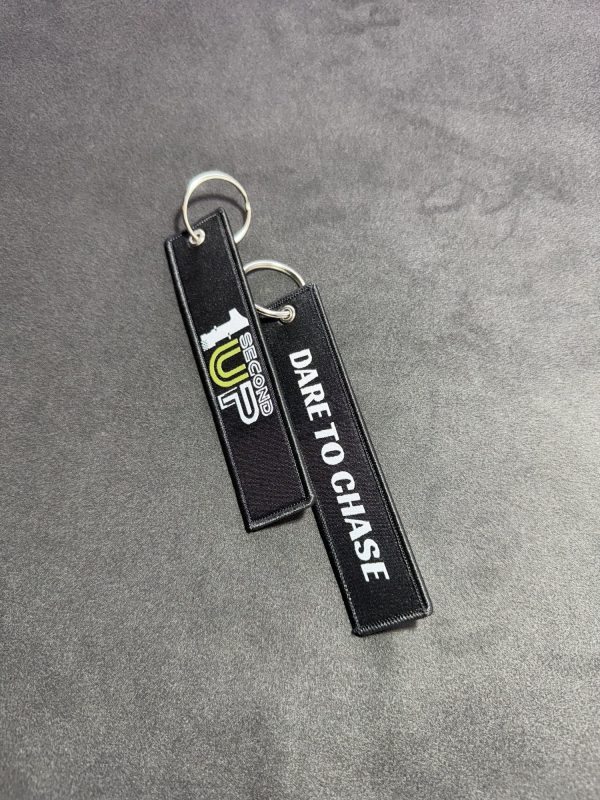 Set of black embroidered Second 1UP motorcycle keychains with 'Dare to Chase' and logo, perfect for motorsports enthusiasts, sideways